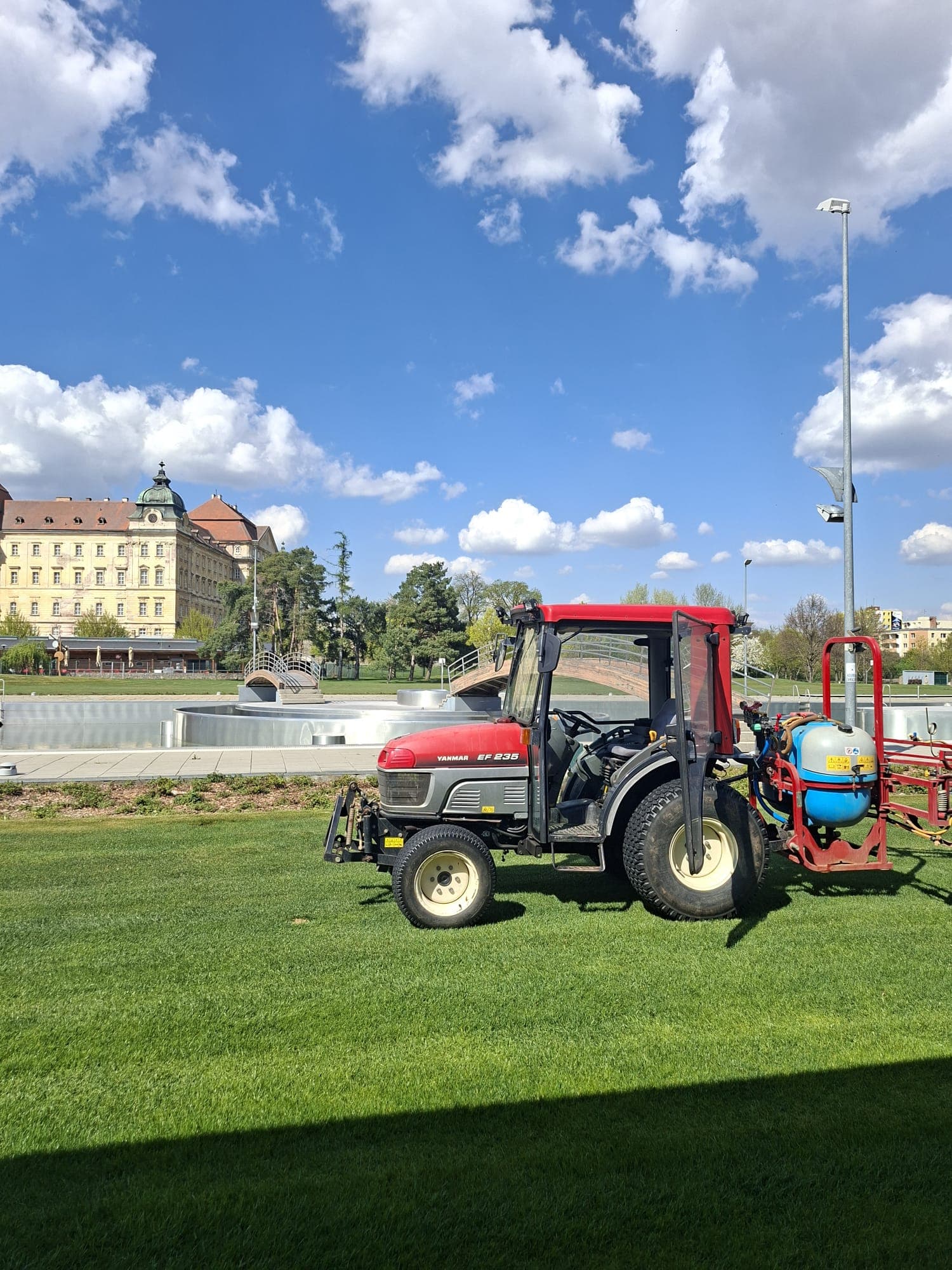 Traktor s postřikovačem na ploše před historickou budovou