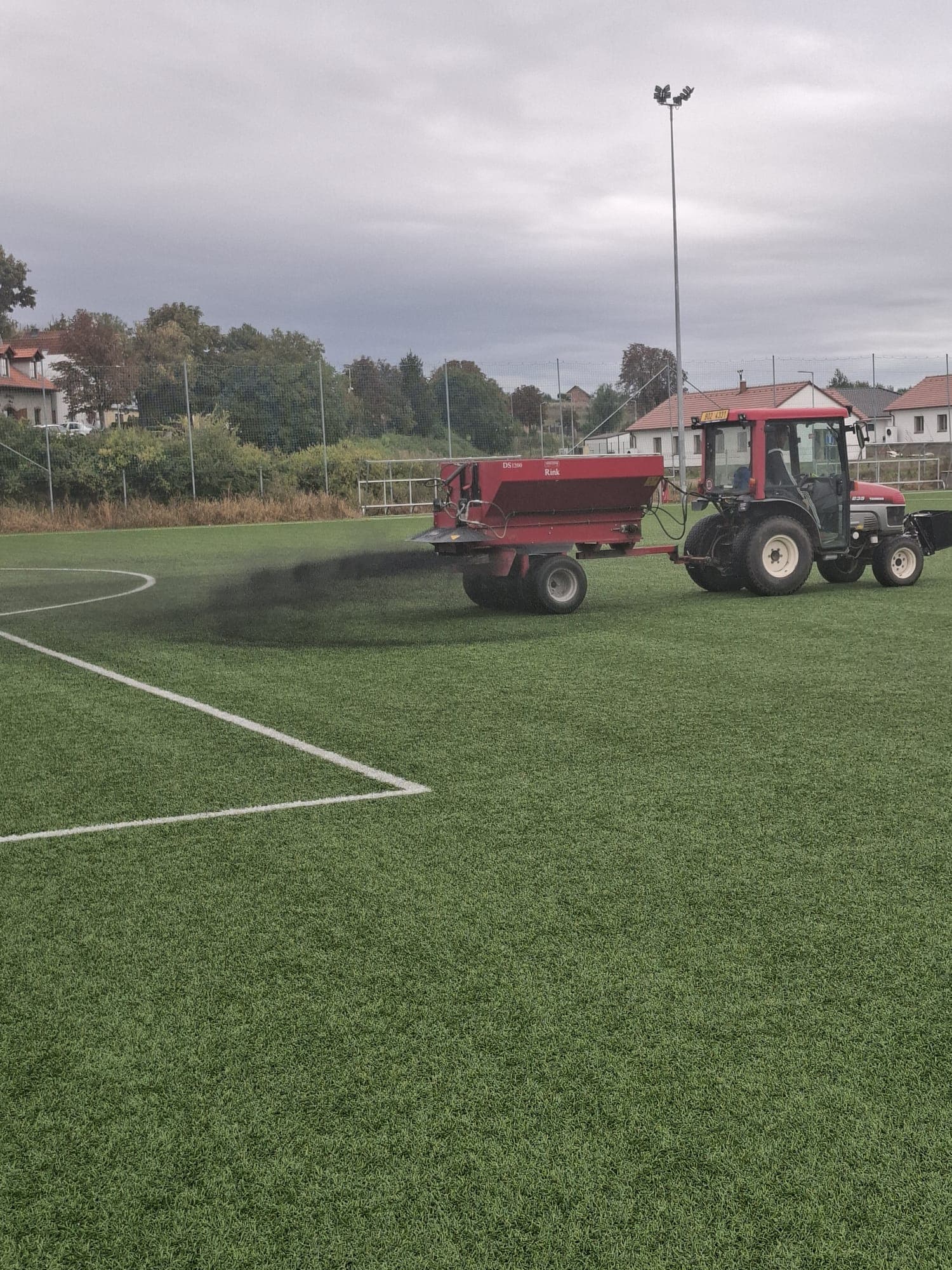Traktor BERK s rozmetadlem při údržbě umělého fotbalového hřiště